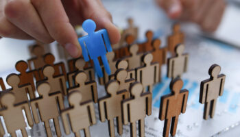 A businessman in blue shirt is holding object in his hand, is searching for personnel or people. Detective looking for missing person crowd of miniature figures choosing most suitable one