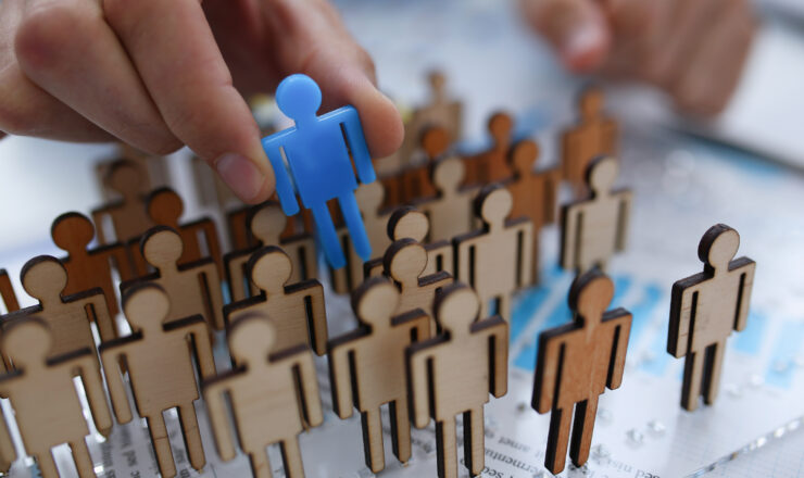 A businessman in blue shirt is holding object in his hand, is searching for personnel or people. Detective looking for missing person crowd of miniature figures choosing most suitable one