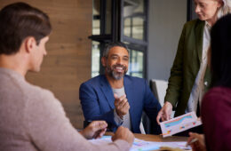 Smiling mid adult indian businessman sharing ideas during a meeting. Engaged team members in a collaborative discussion. Positive business meeting with teamwork and strategy planning.